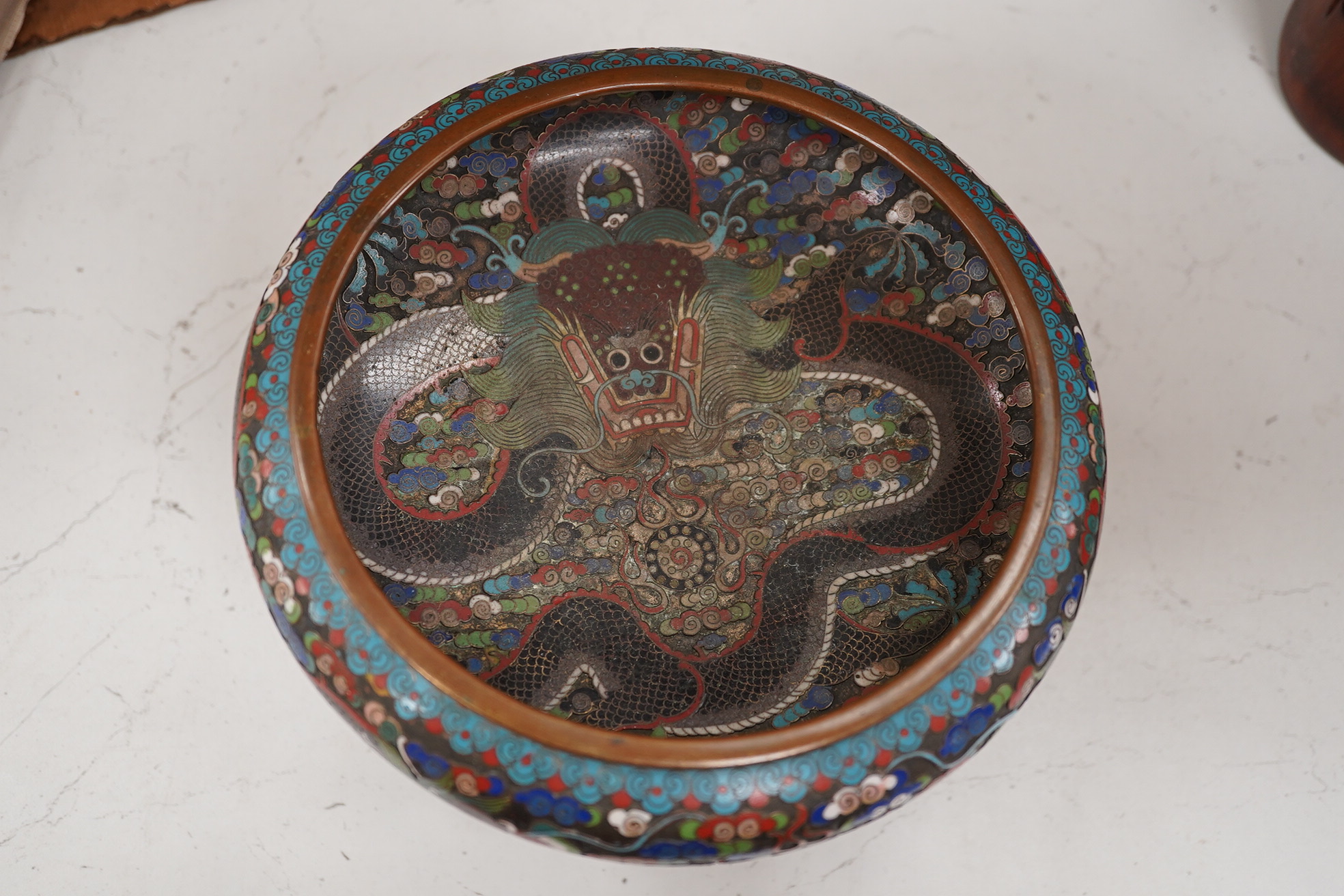 A Chinese cloisonné enamel ‘dragon’ bowl, Qianlong mark but early 20th century, on hardwood stand, 20cm diameter. Condition - poor to fair